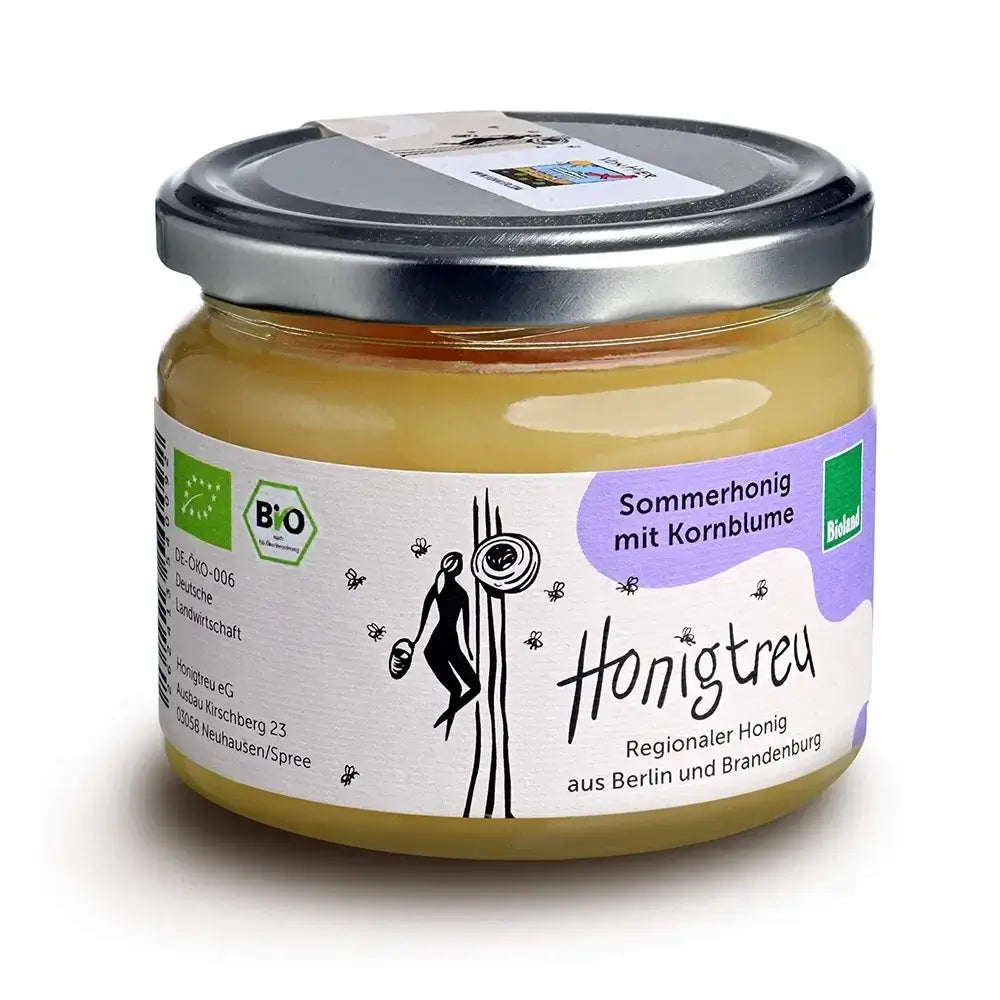 Ein 360g-Glas cremiger Bio-Sommerhonig mit Kornblume von Honigtreu. Der Honig hat eine hellgelbe, feine Konsistenz. Das Etikett ist lila-weiß gestaltet und mit dem Bioland-Logo versehen.